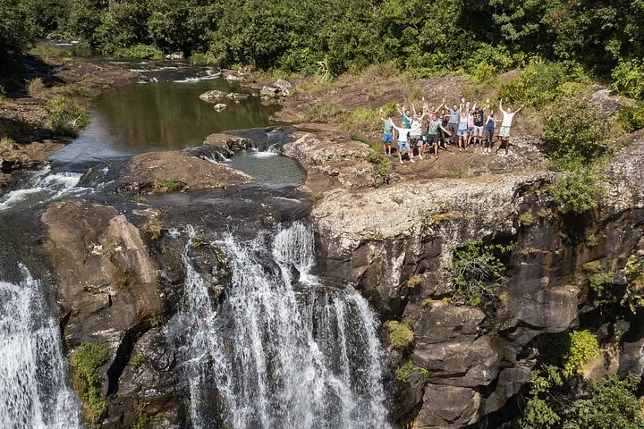 Eine große Gruppe Wanderer winkt vom oberen Rand eines Wasserfalls