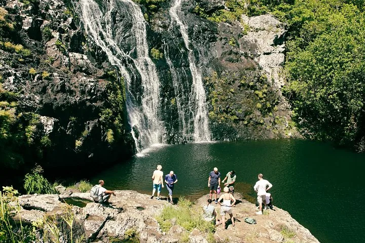 Eine Gruppe Menschen versammelt sich um ein Becken am Fuß eines Wasserfalls
